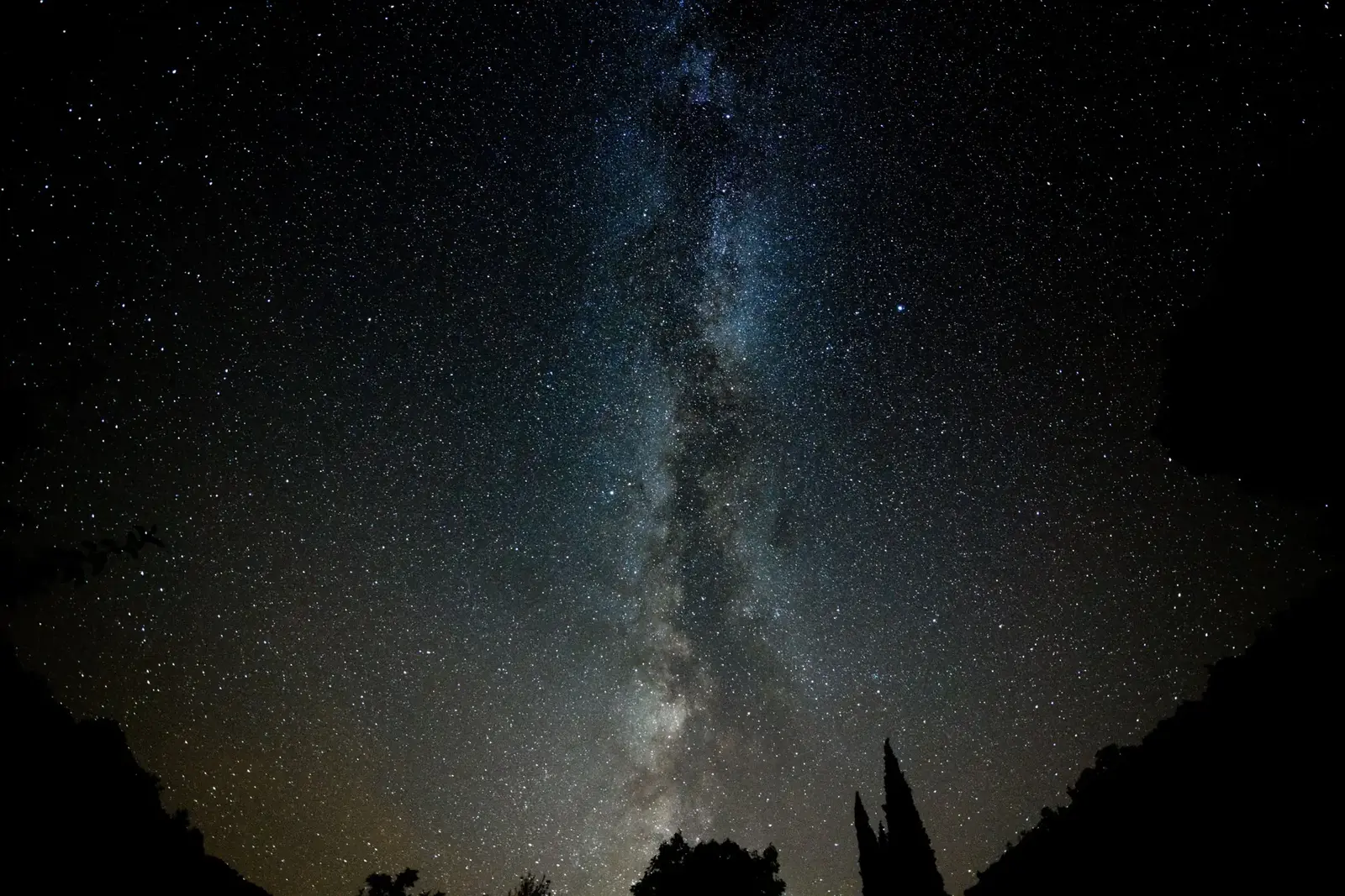 The Milky Way and the Magellanic Clouds arching over a dark ridge in a night sky free of light pollution