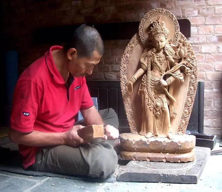 A Nepali woodcarver shaping a sacred figure on a lotus base by hand with a mallet and chisel